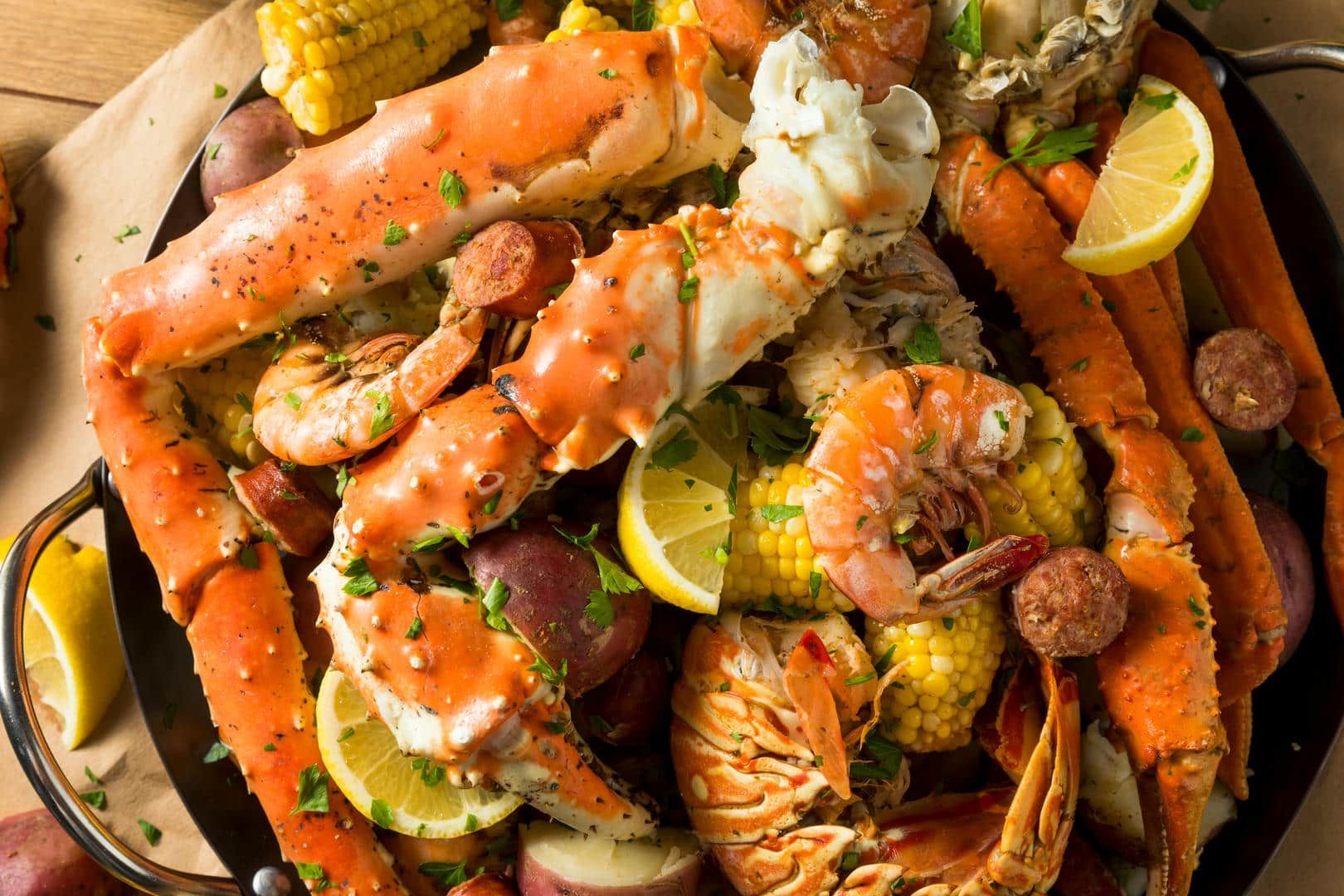 A pan filled with crab legs , shrimp , corn , potatoes and sausage.