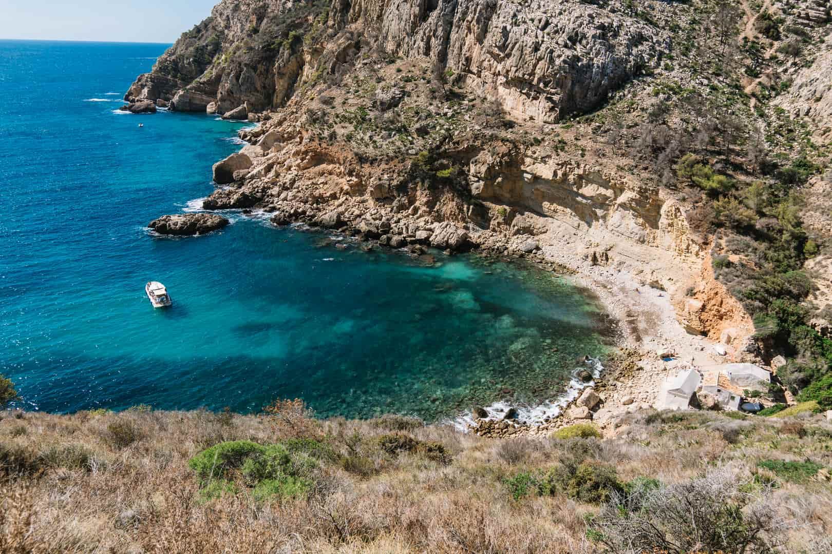 A boat is floating on top of a body of water next to a cliff.