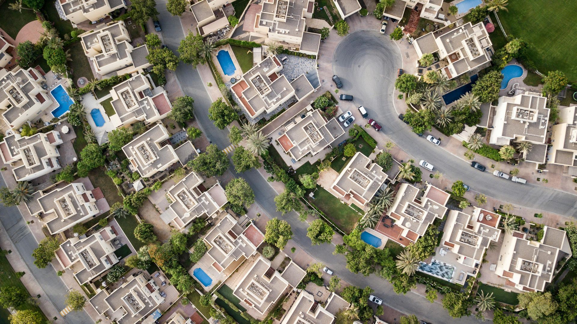 Aerial view of a suburban neighborhood with houses, pools, roads, and trees.
