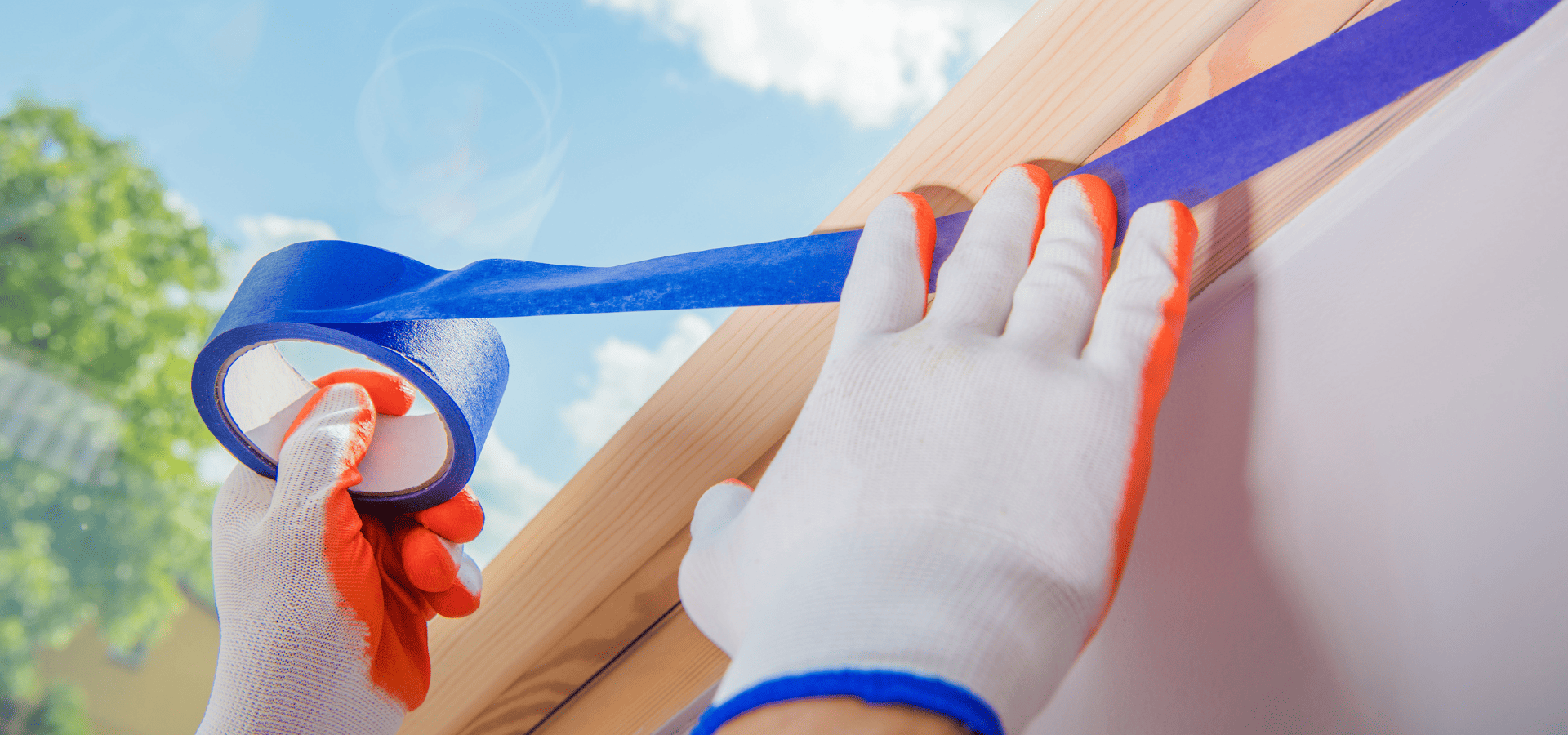 Applying blue painter's tape to the edges of the wooden exterior of a mobile home