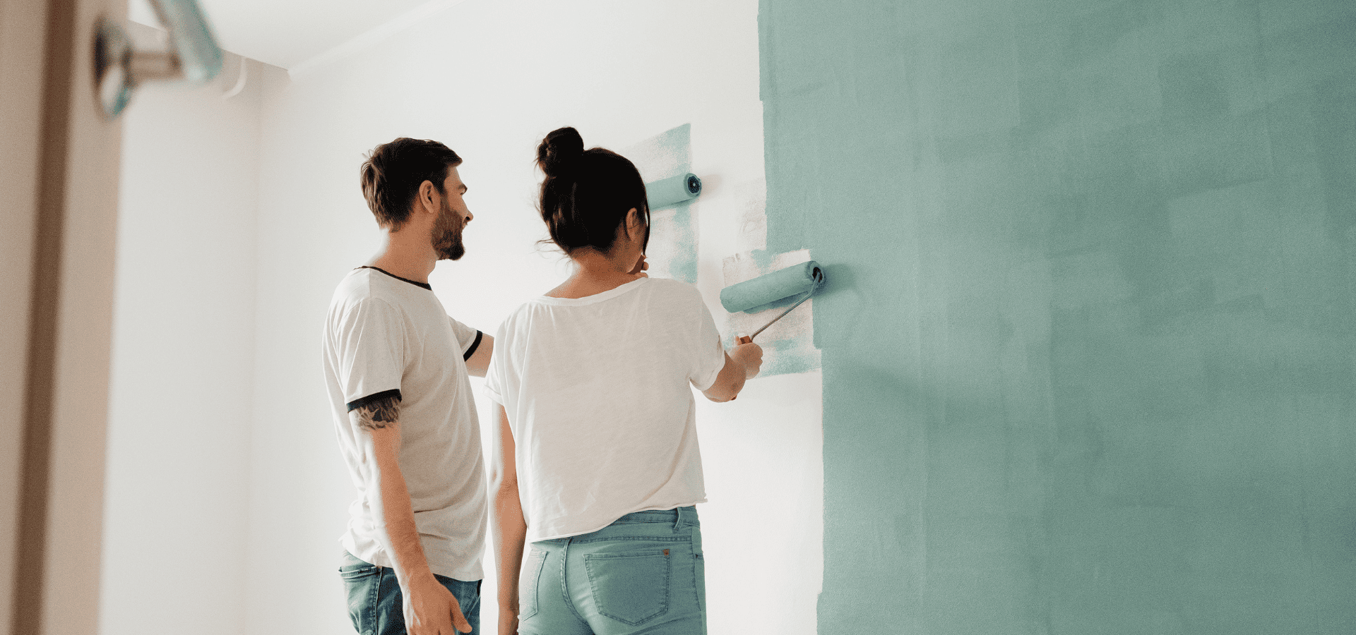 Couple painting their home walls with green paint using rollers