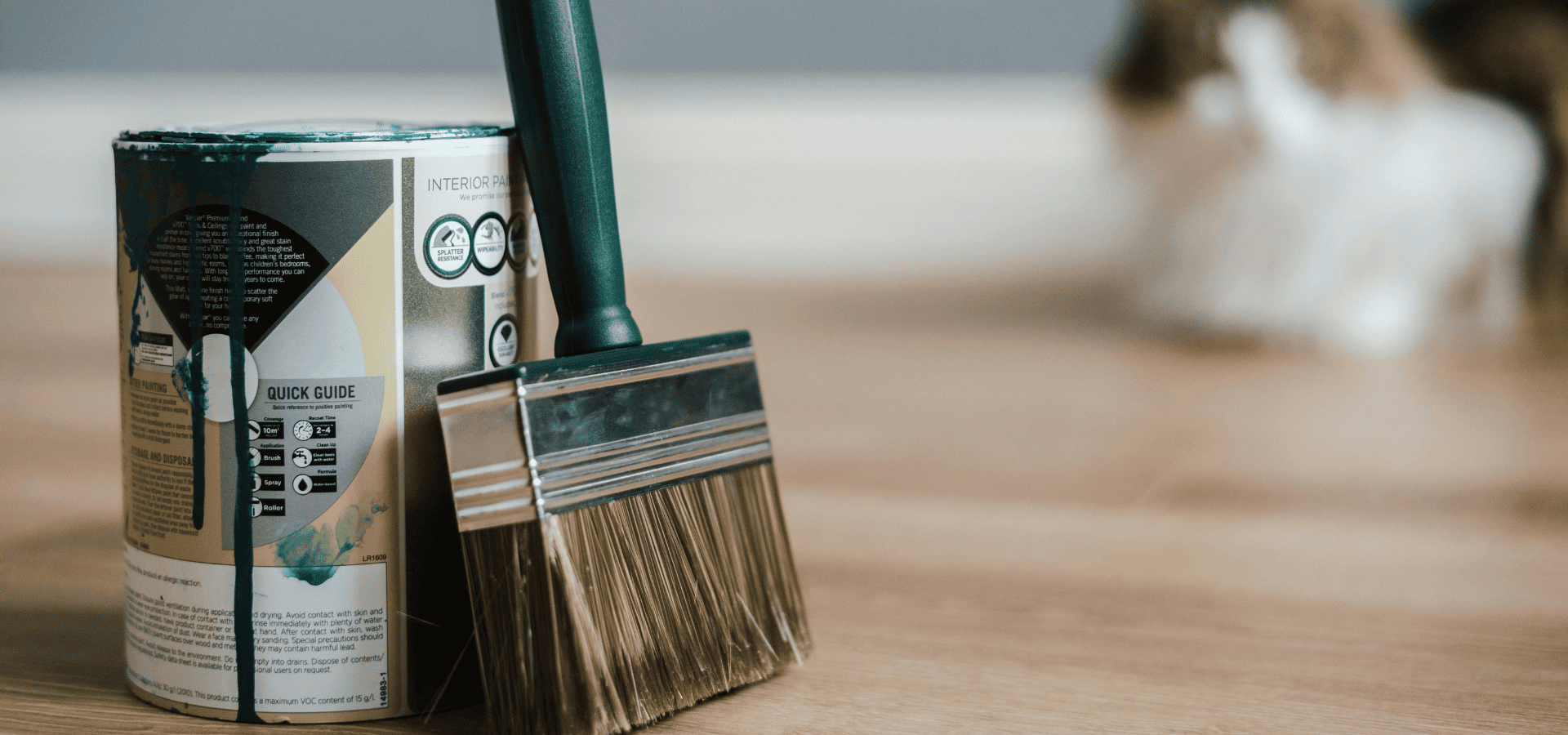 A can of dark green interior paint with a dark green paintbrush beside it