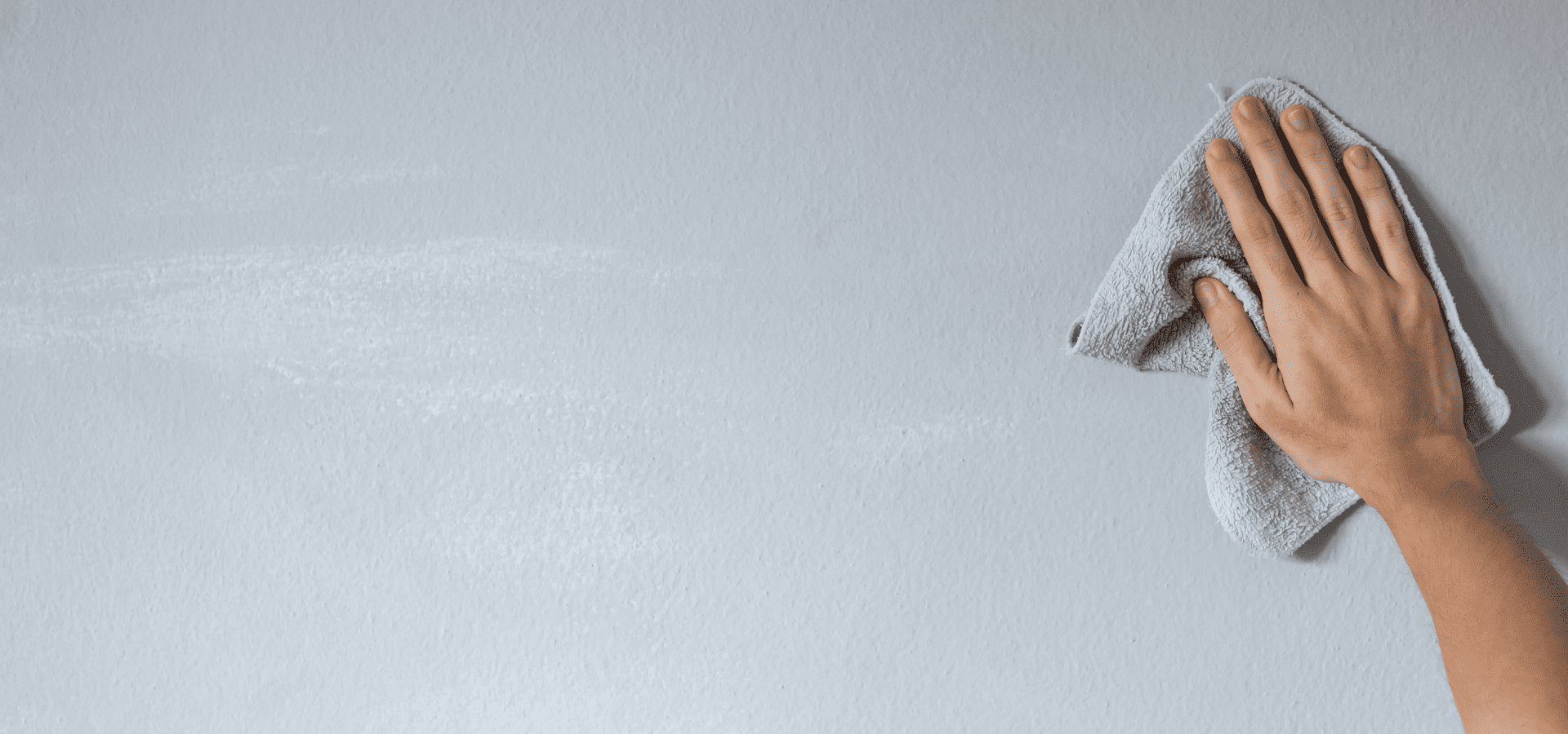 Dusting a painted wall with a microfiber cloth to remove dust, dirt, cobwebs, and debris