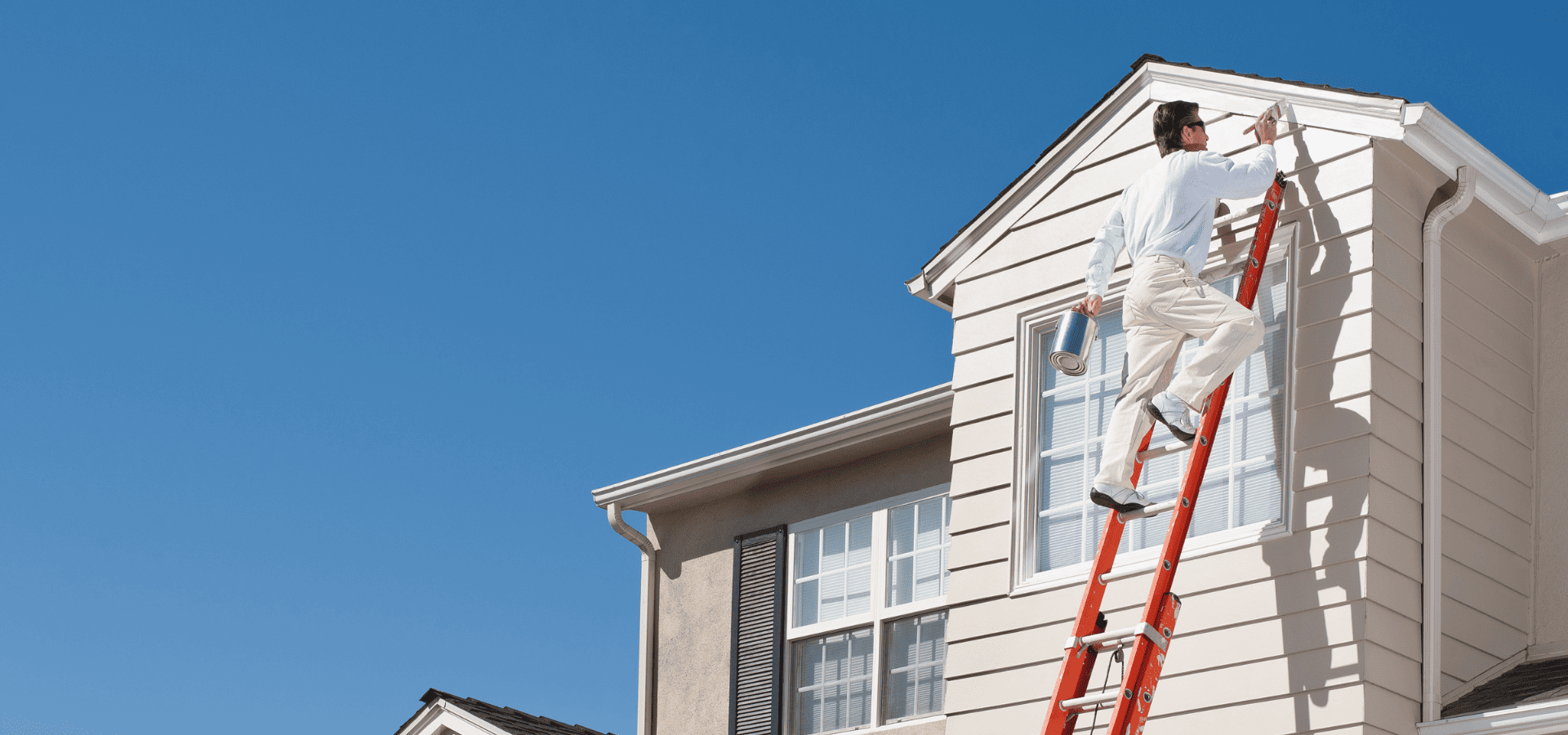 A homeowner on a ladder painting his home exterior to prepare it for resale