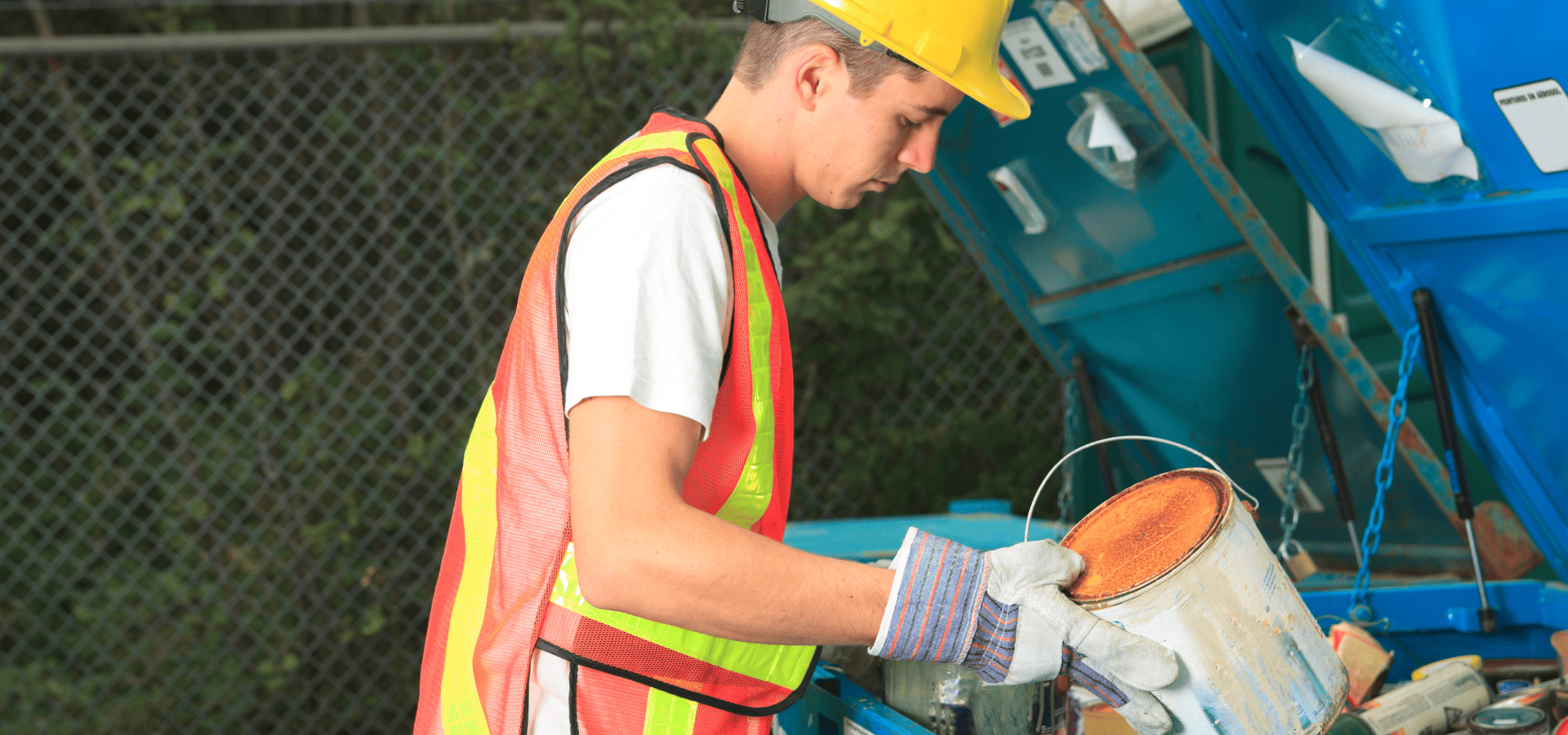 Paint recycling site worker holding a can of orange paint from the recycling site