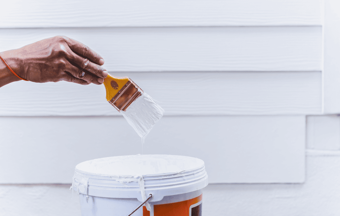 A painter from Renewed Walls Painting holding up a paint brush while painting the exterior of a client's house