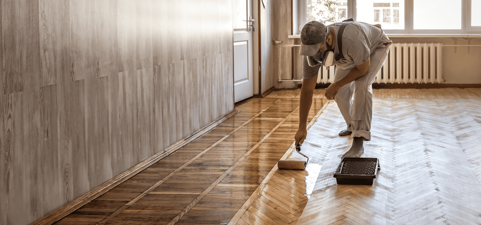 Painter from Renewed Walls Painting using a roller to apply floor paint onto wooden flooring
