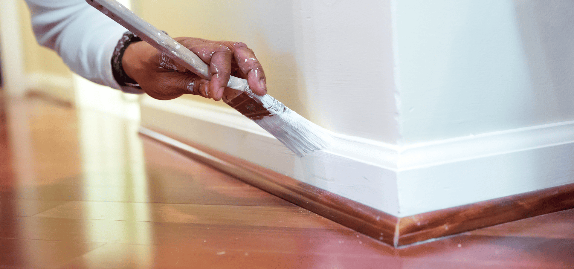 Worker from Renewed Walls Painting painting the baseboard of a home with glossy paint