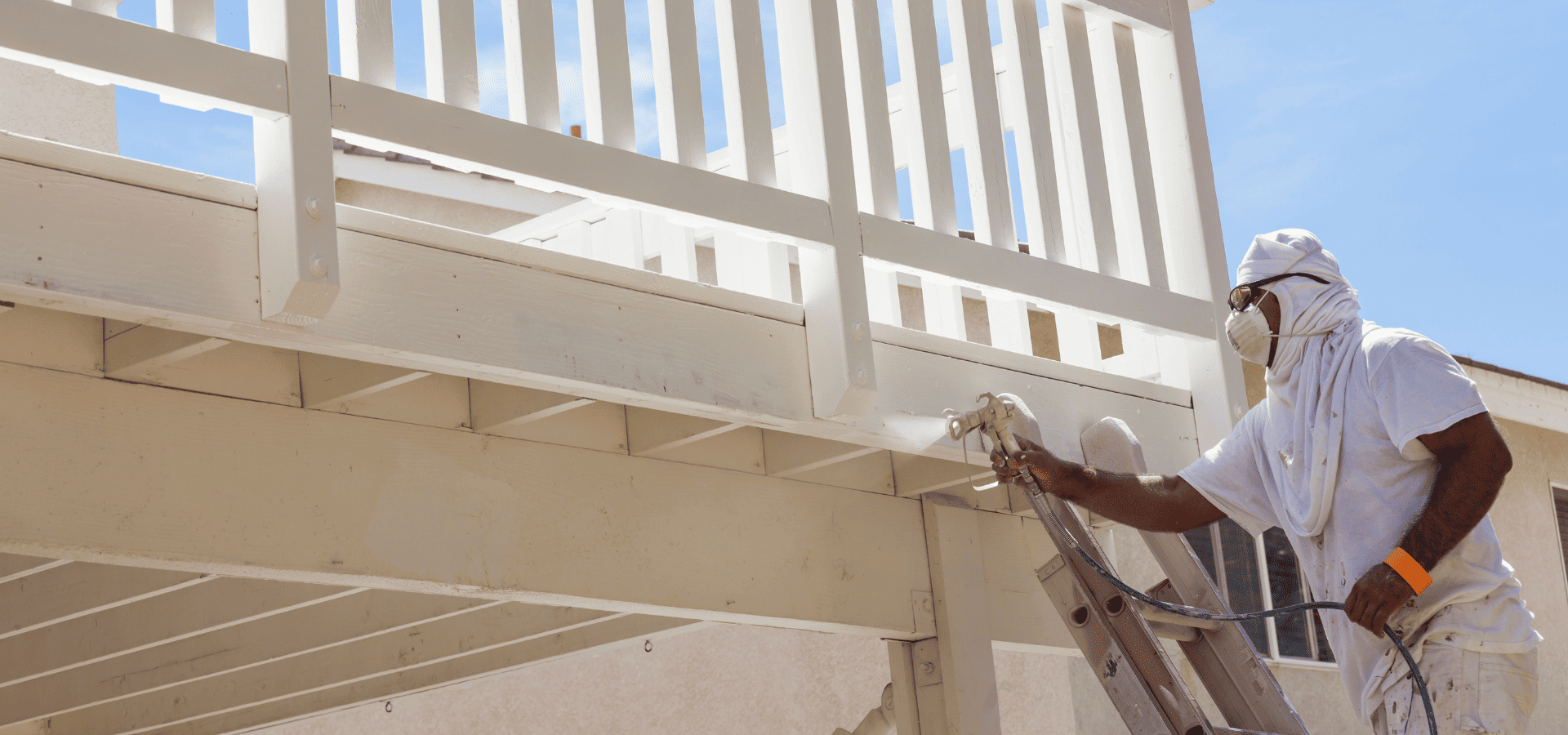 Worker spraying white paint on the bottom of a balcony in Raleigh, NC