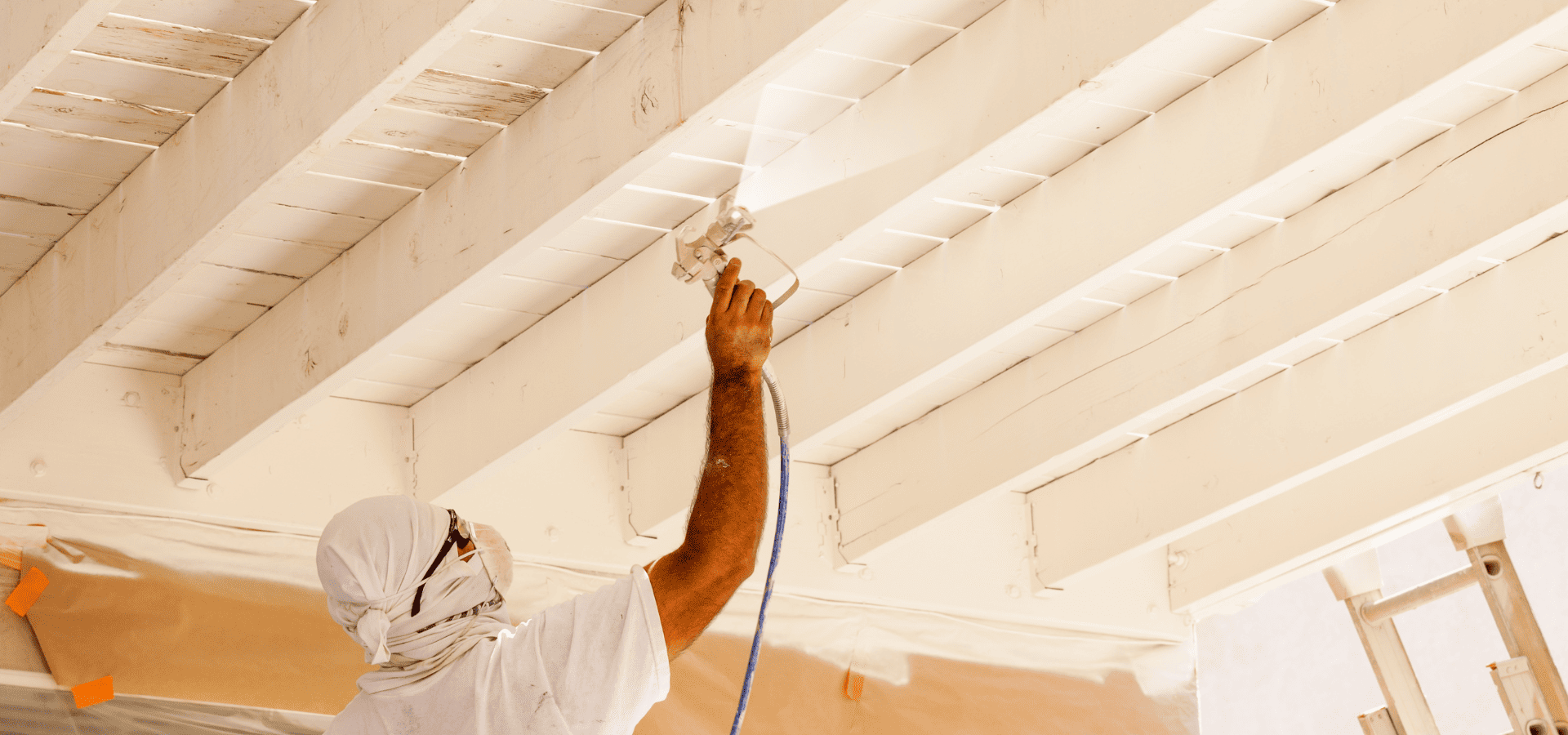 A worker spraying paint on the interior ceiling of a house that's under construction