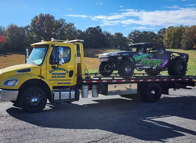 Yellow tow truck transports a decorated off-road vehicle on a sunny day.