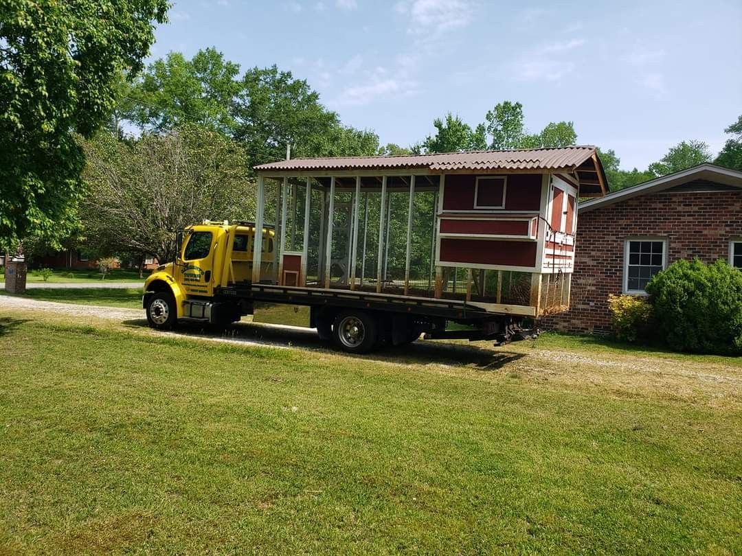 Yellow flatbed truck transporting a red and white chicken coop on a grassy lawn.