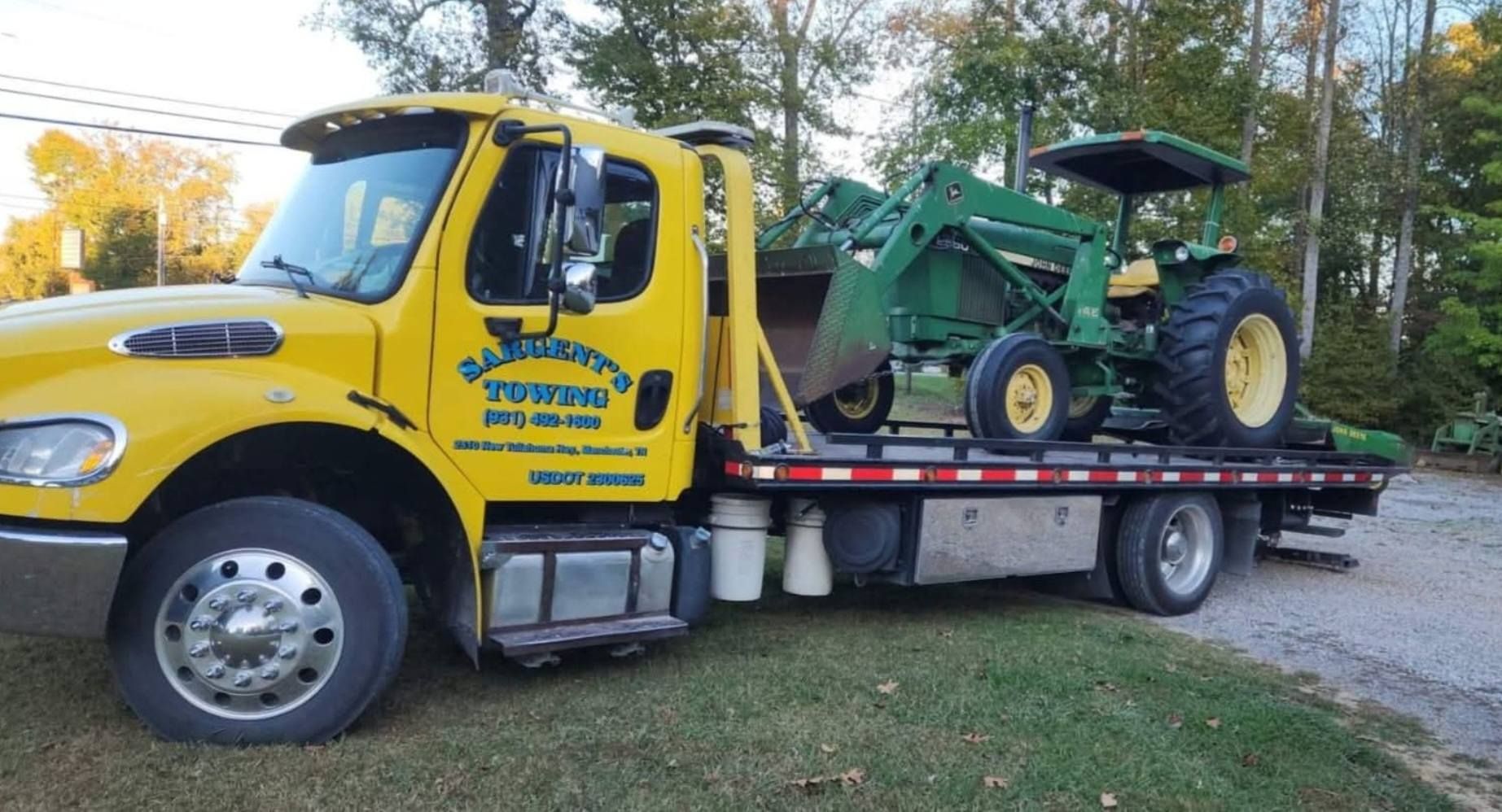 Yellow tow truck transporting a green and yellow tractor with a front loader.
