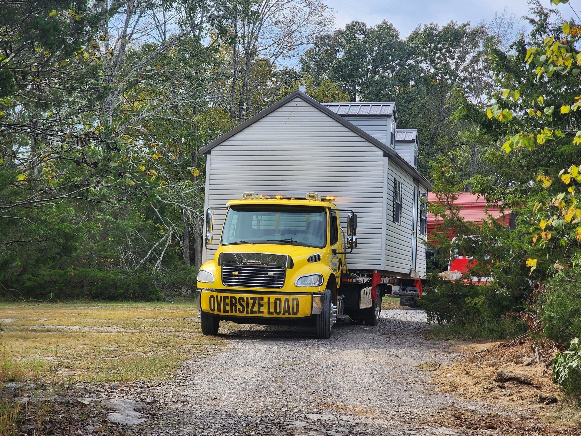 Yellow truck transporting a small house on a rural road;