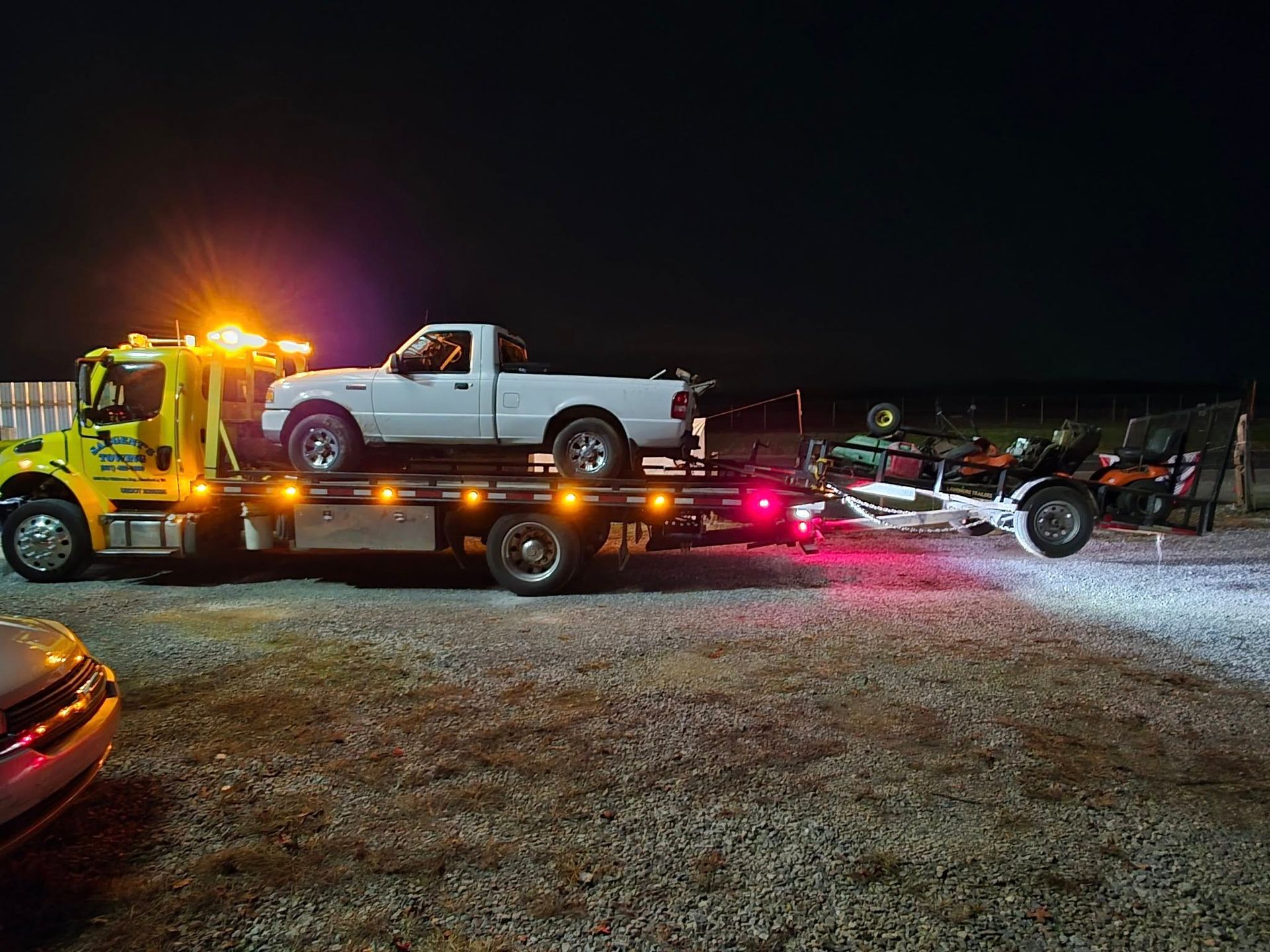 A white pickup truck and a trailer with two ATVs being towed by a yellow tow truck at night.
