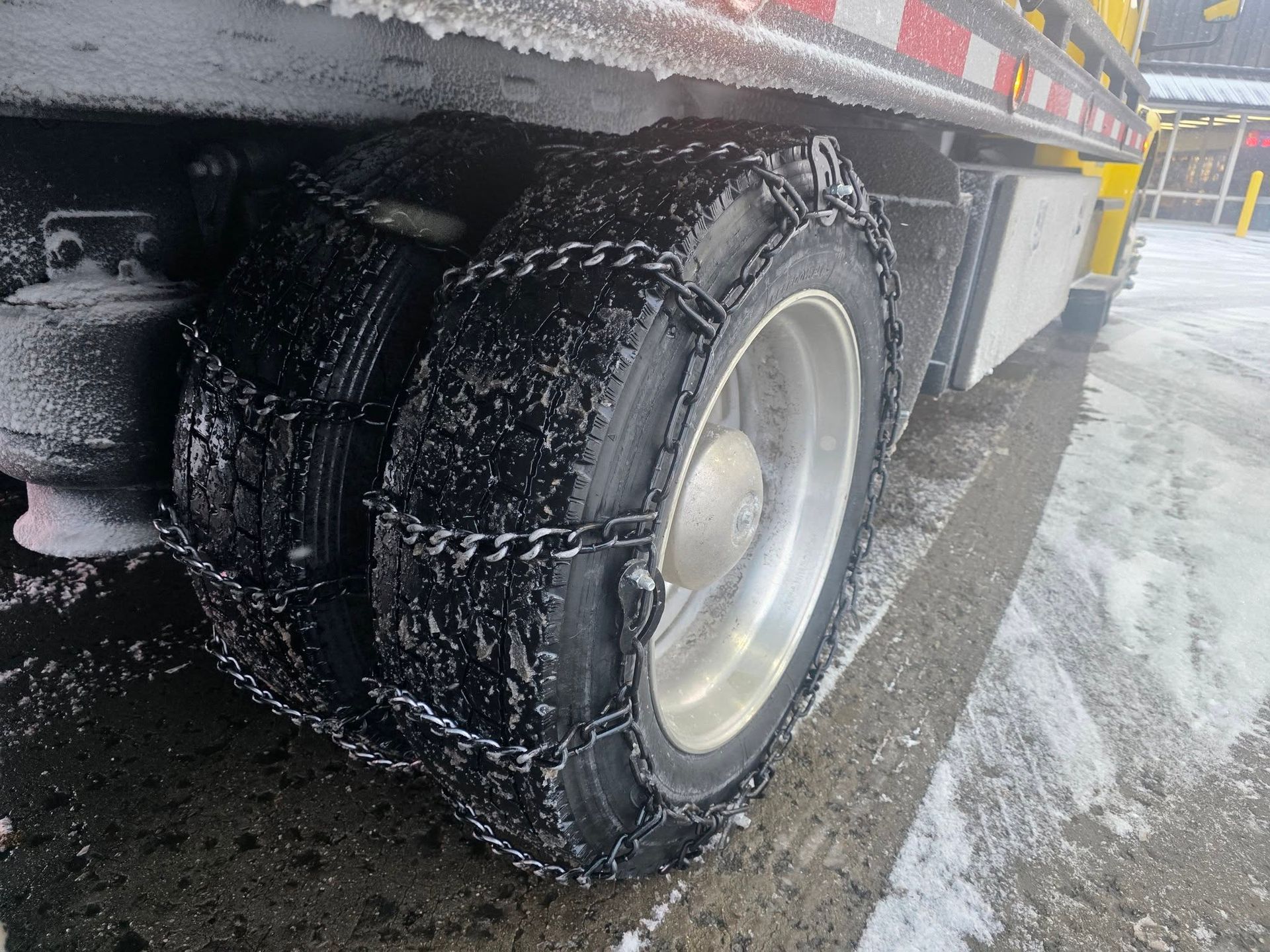 Semi-truck tires with chains, covered in snow, on a wet, snow-covered road.