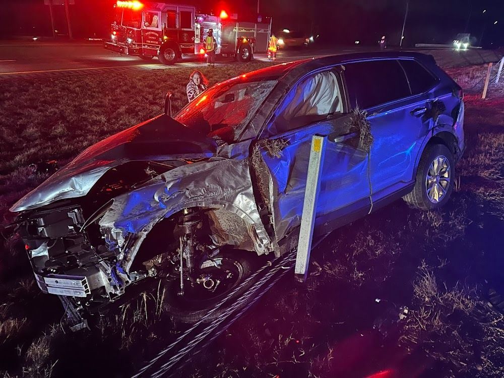 Damaged blue SUV at night with emergency vehicles in the background. Crash scene.