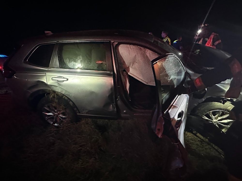 Car accident at night; SUV with deployed airbags, damaged door, and emergency personnel nearby.