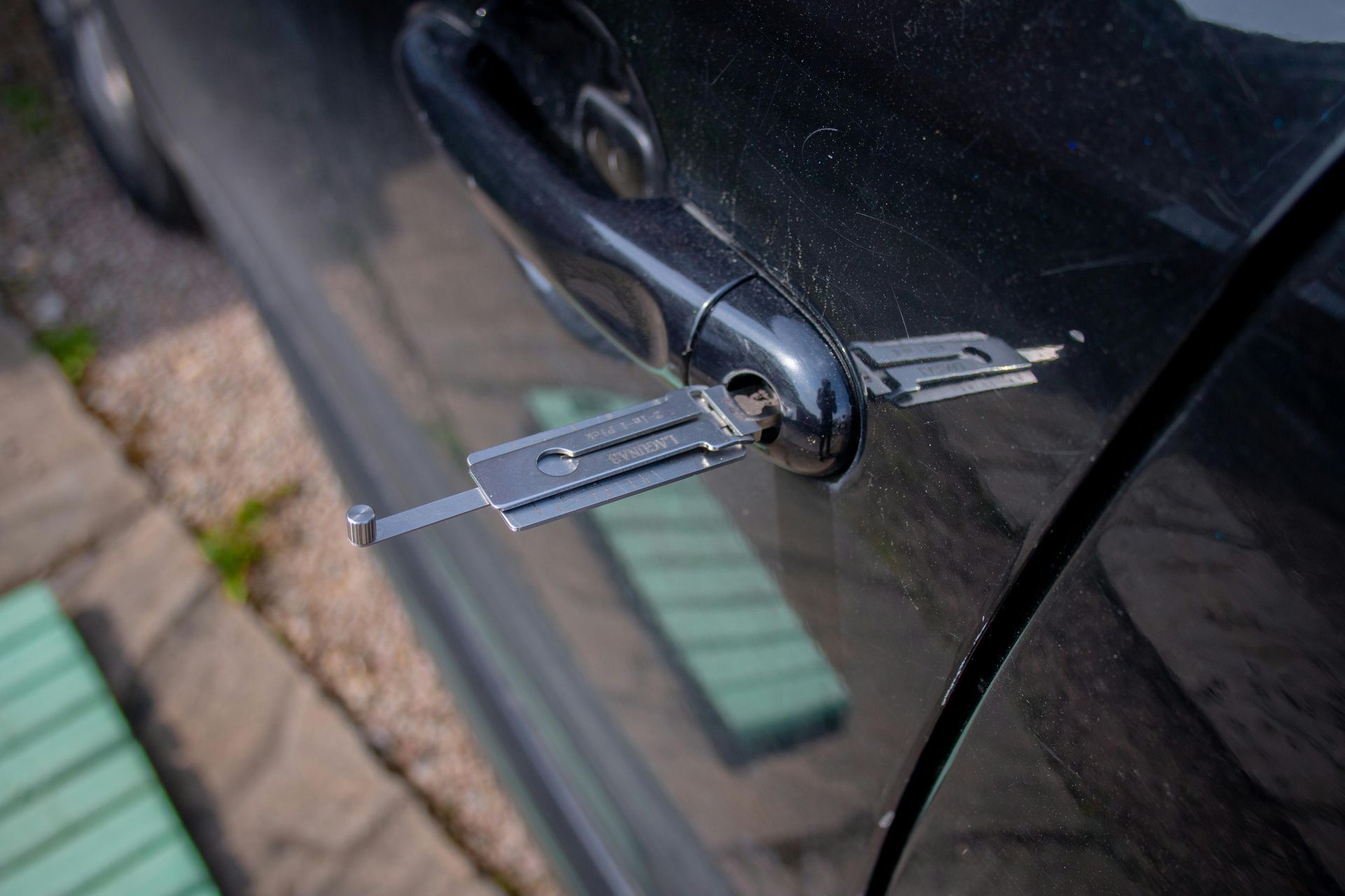 Lock pick tool inserted into a black car door handle, attempting to unlock the door.