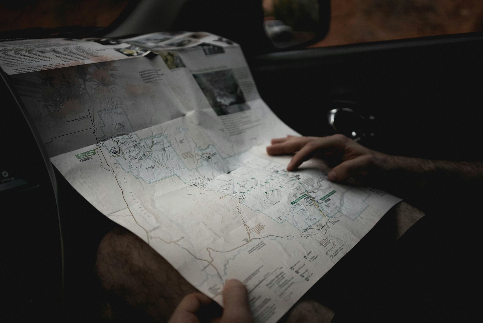 Hands holding and studying a map inside a vehicle. The map has roads, trails, and features marked.
