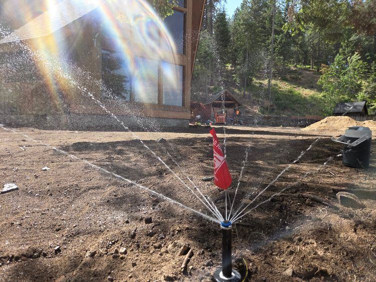 A sprinkler is spraying water on a dirt field in front of a house.
