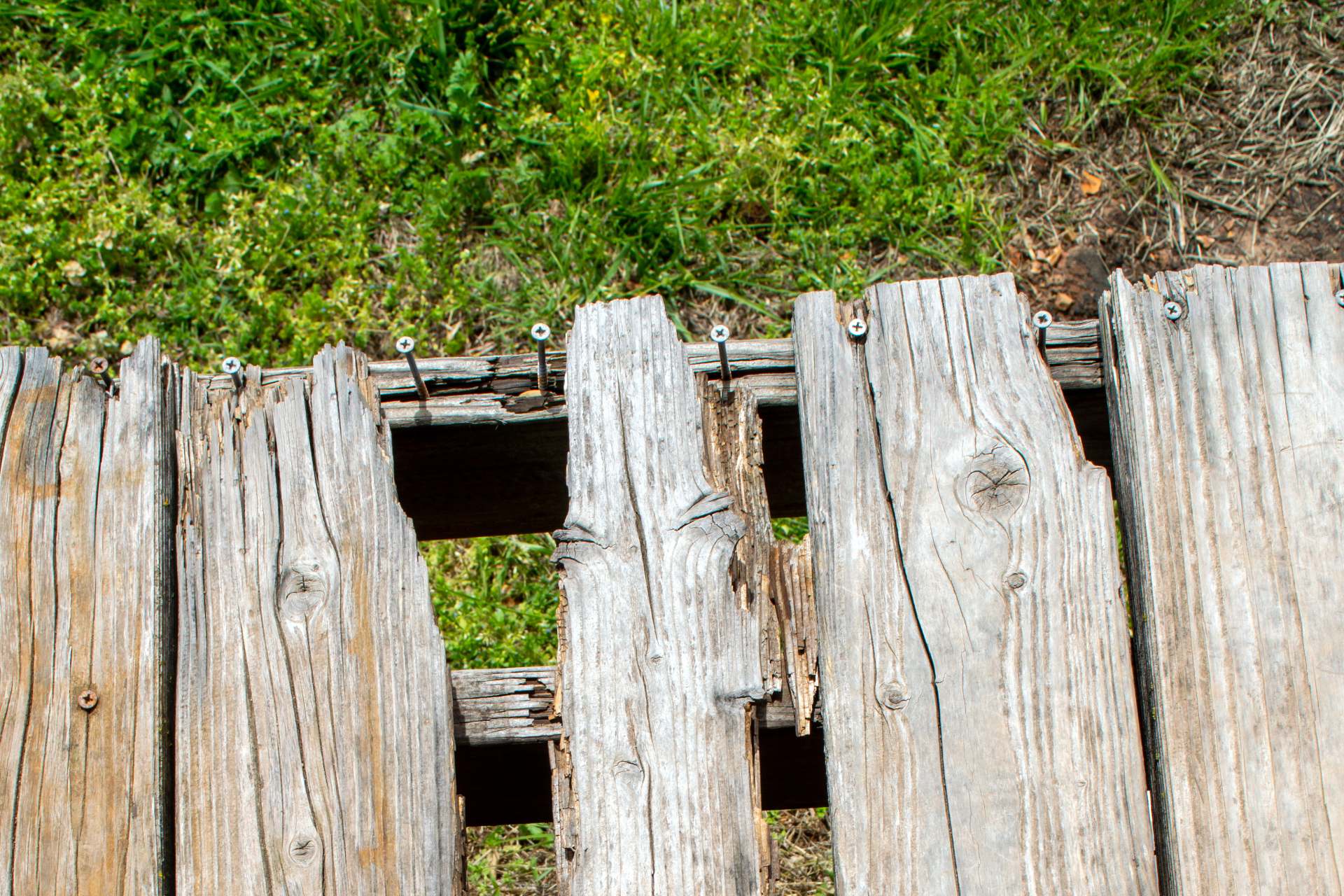 A photo of an old, worn-down deck that desperately needs repair or replacement. The deck panels are dried, warped, cracked, and missing bits and pieces. This is incredibly unsafe and needs to be replaced/repaired immediately.