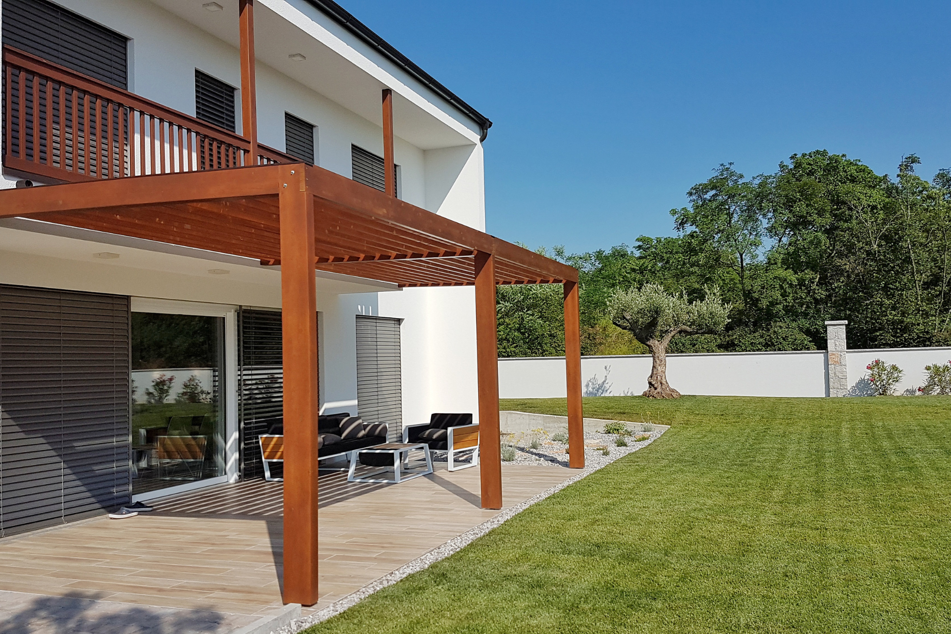 A  photo of a newly installed pergola attached to the house's frame. The pergola sits on a concrete and gravel slab and covers almost 75 percent of the patio.