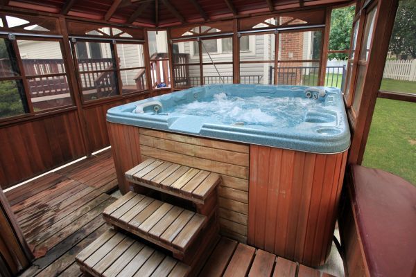 A hot tub with bubbling water on a wooden deck, enclosed by a gazebo, in a backyard.