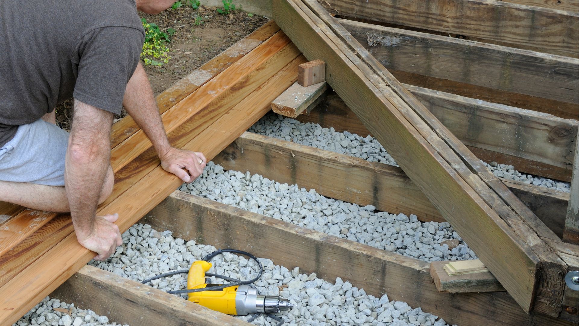 Man building a wooden deck with power tools and gravel base in Stockton, CA.