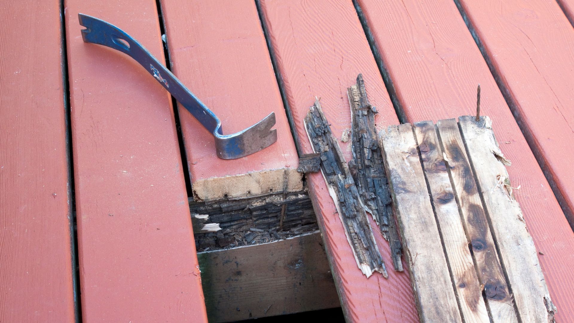 Deck repair in progress in Stockton, CA, with removed rotten boards and a pry bar on a red-painted d