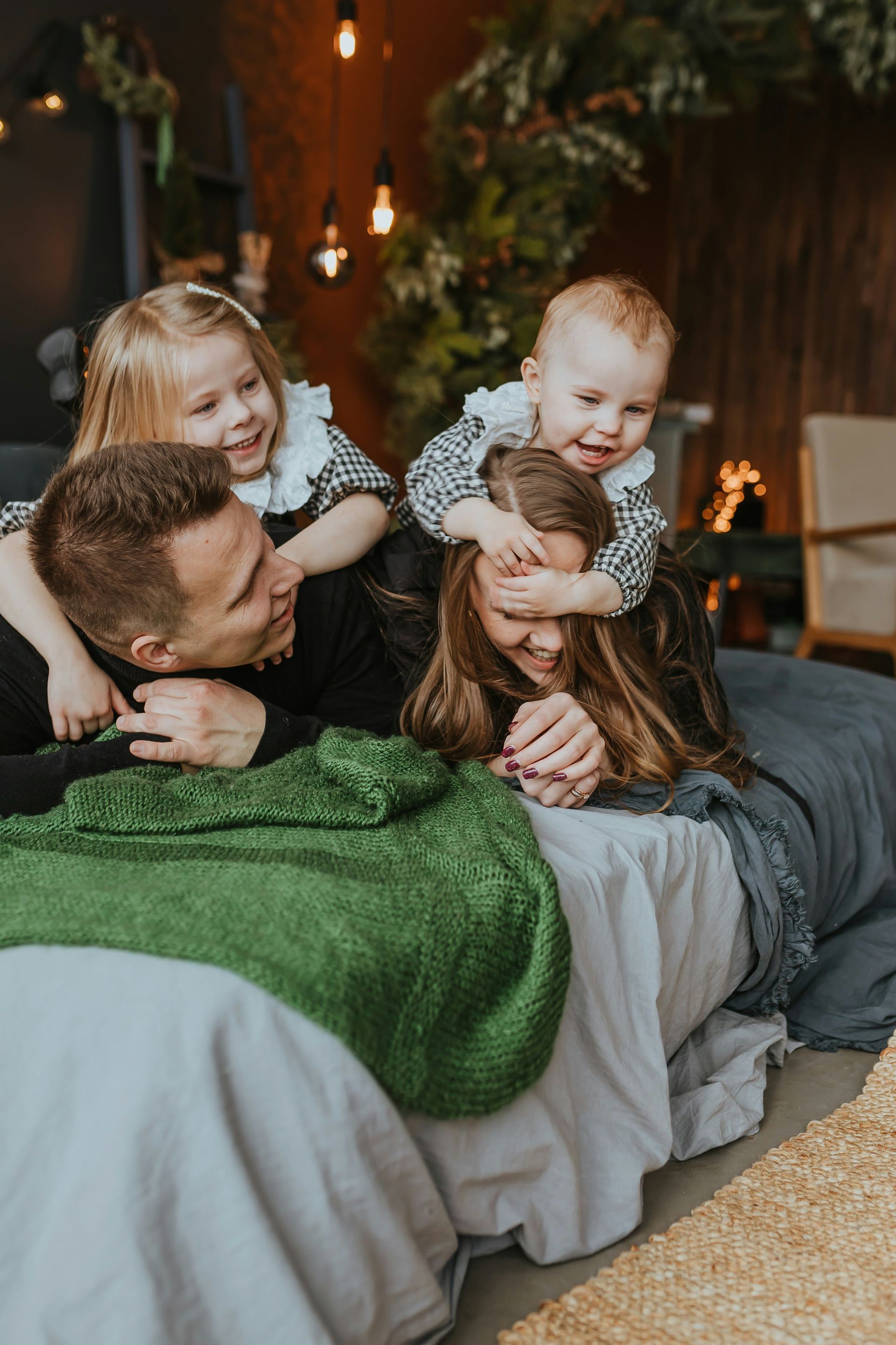 A family is laying on a bed with a christmas tree in the background.