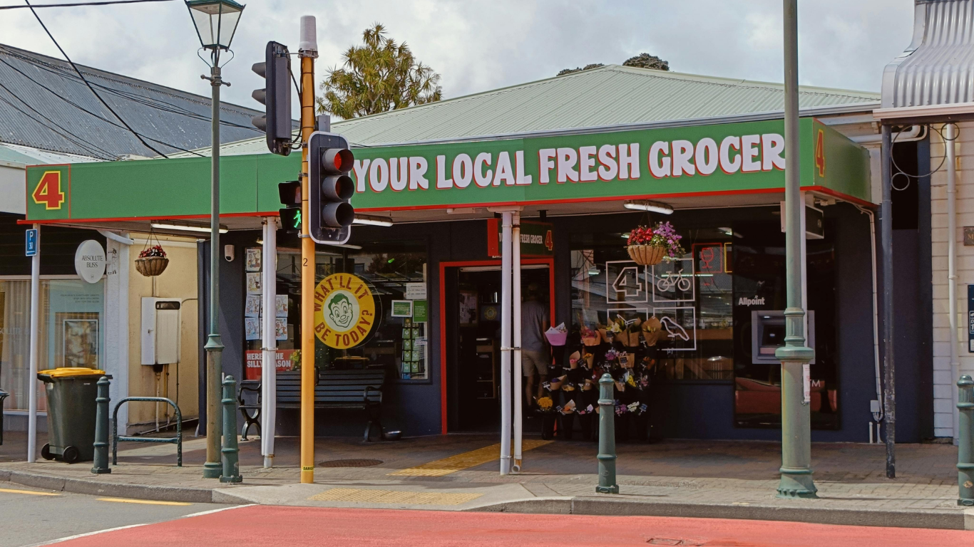 Green-roofed grocery store on a street corner, sign says