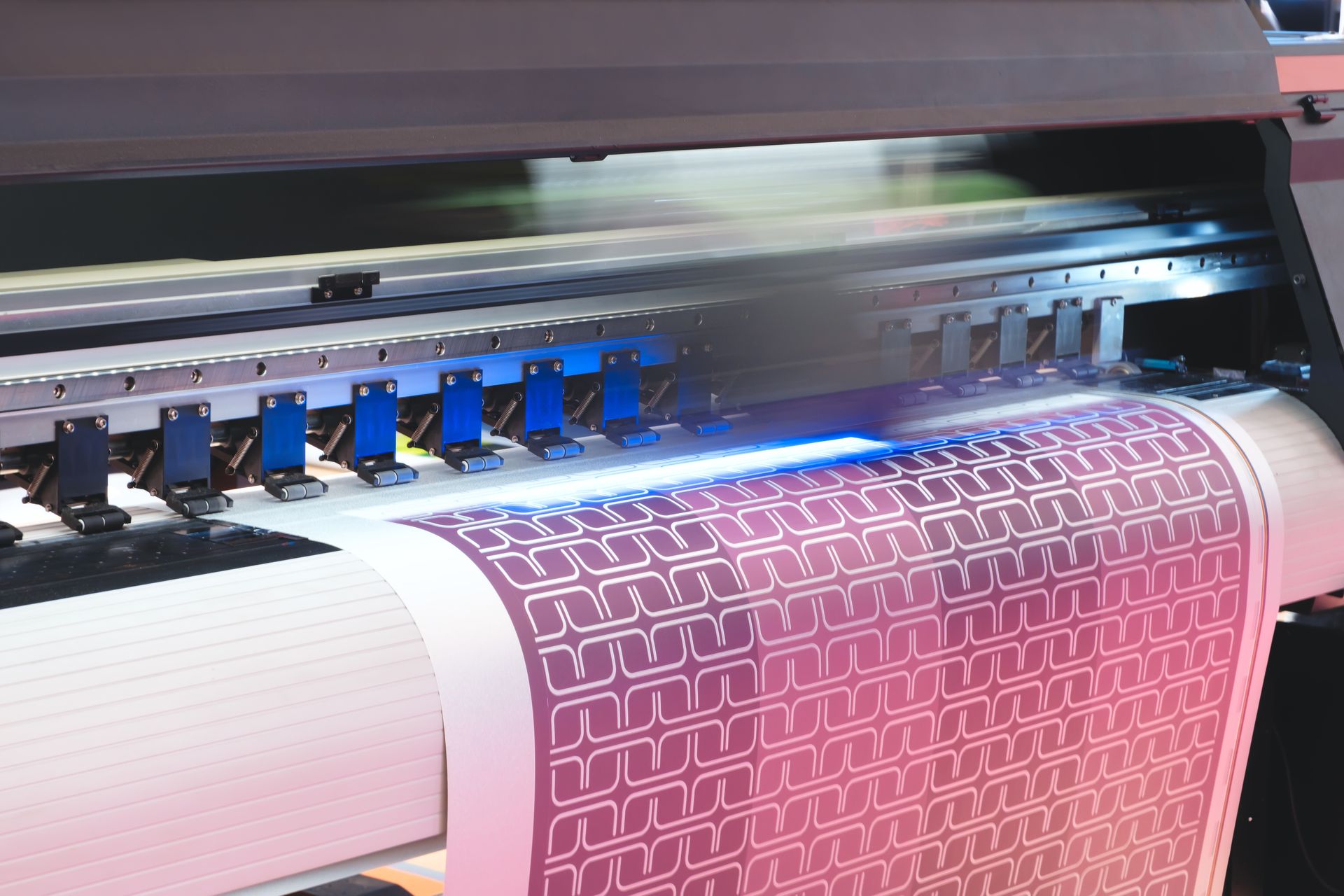 Large-format printer printing a pink and white patterned design on a roll of paper.