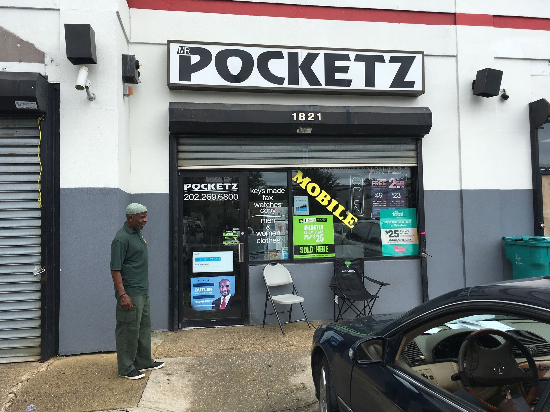 A shop called Pocketz with a man in green standing outside. A car is parked to the right.