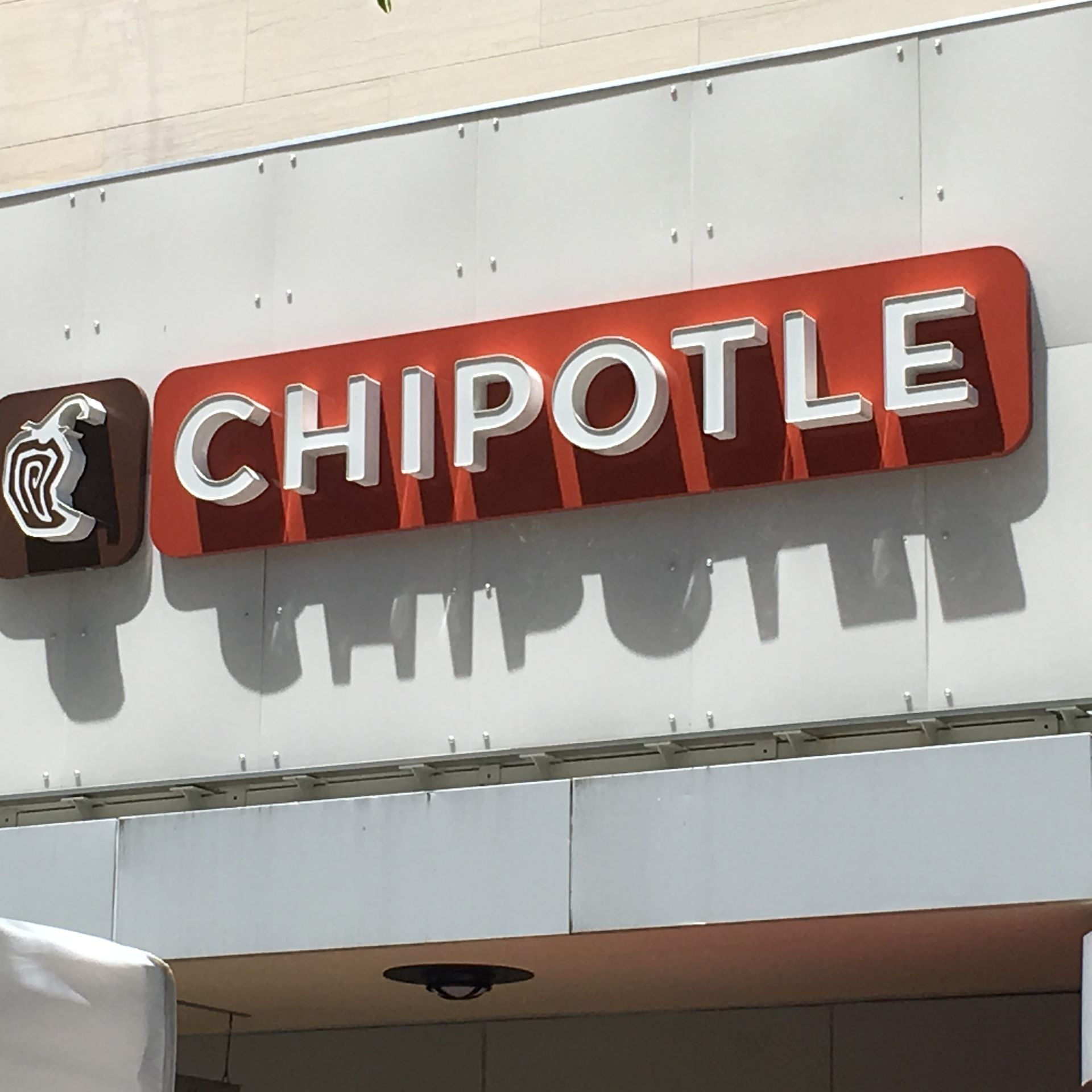 Chipotle restaurant sign with white letters on a red rectangle and a brown logo; outdoors.