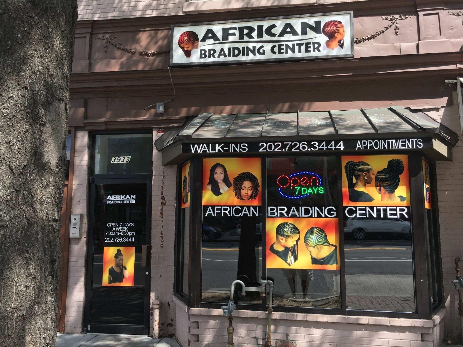 Exterior of African Braiding Center storefront, with sign, window displays featuring braided hairstyles, and phone number.