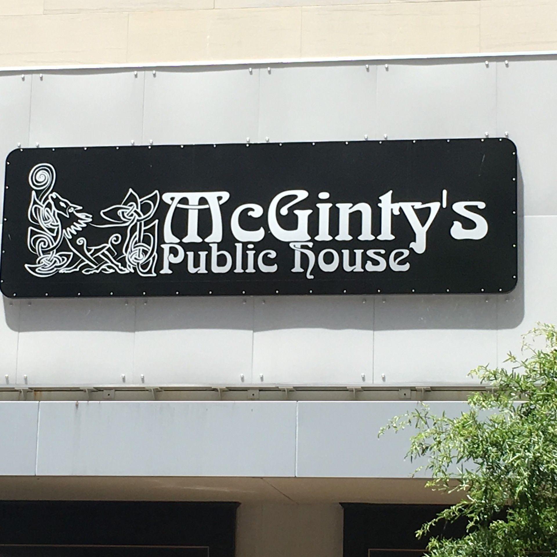 Black sign for McGinty's Public House with white lettering and Celtic-style design, mounted on a building.