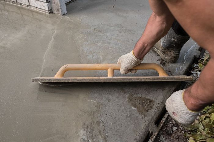 A man is using a trowel to level a concrete floor.