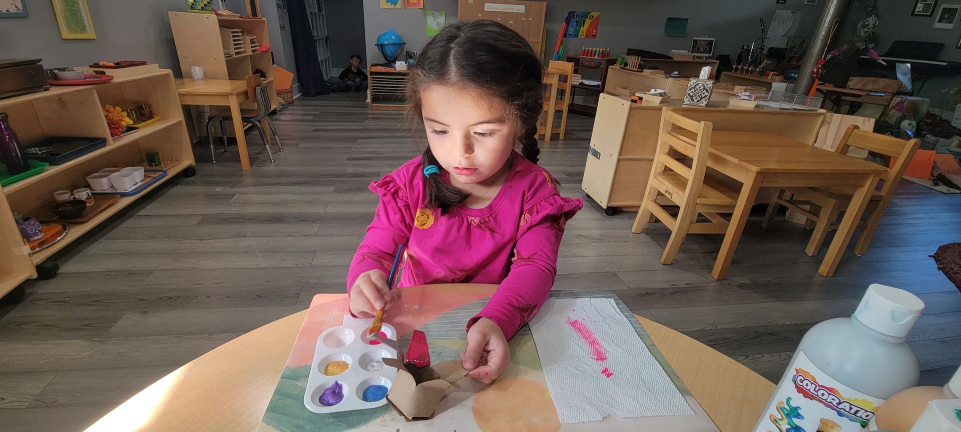 Young child seated at a table paintin a picture.