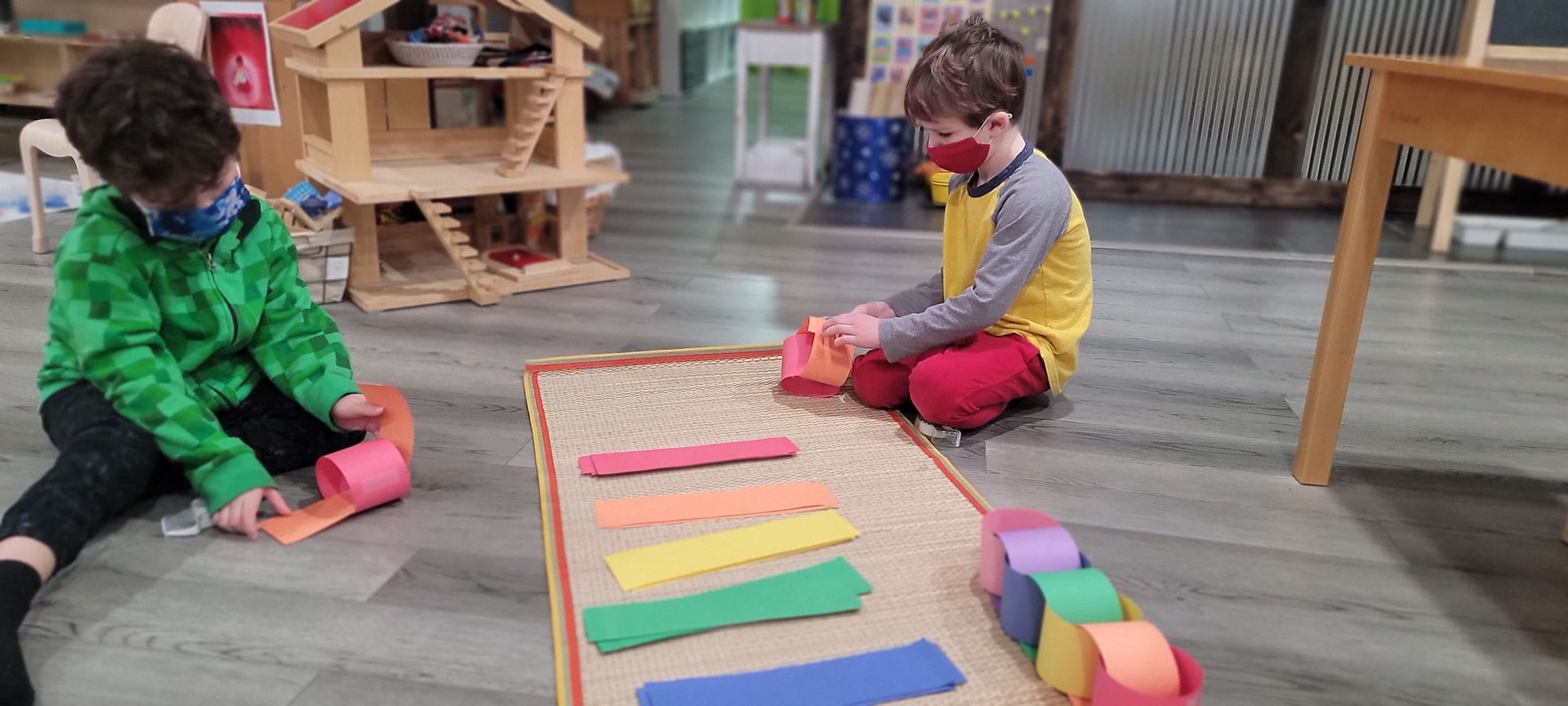 A child sits on the floor, busy with making paper chains from an assortment of colored strips of construction paper.