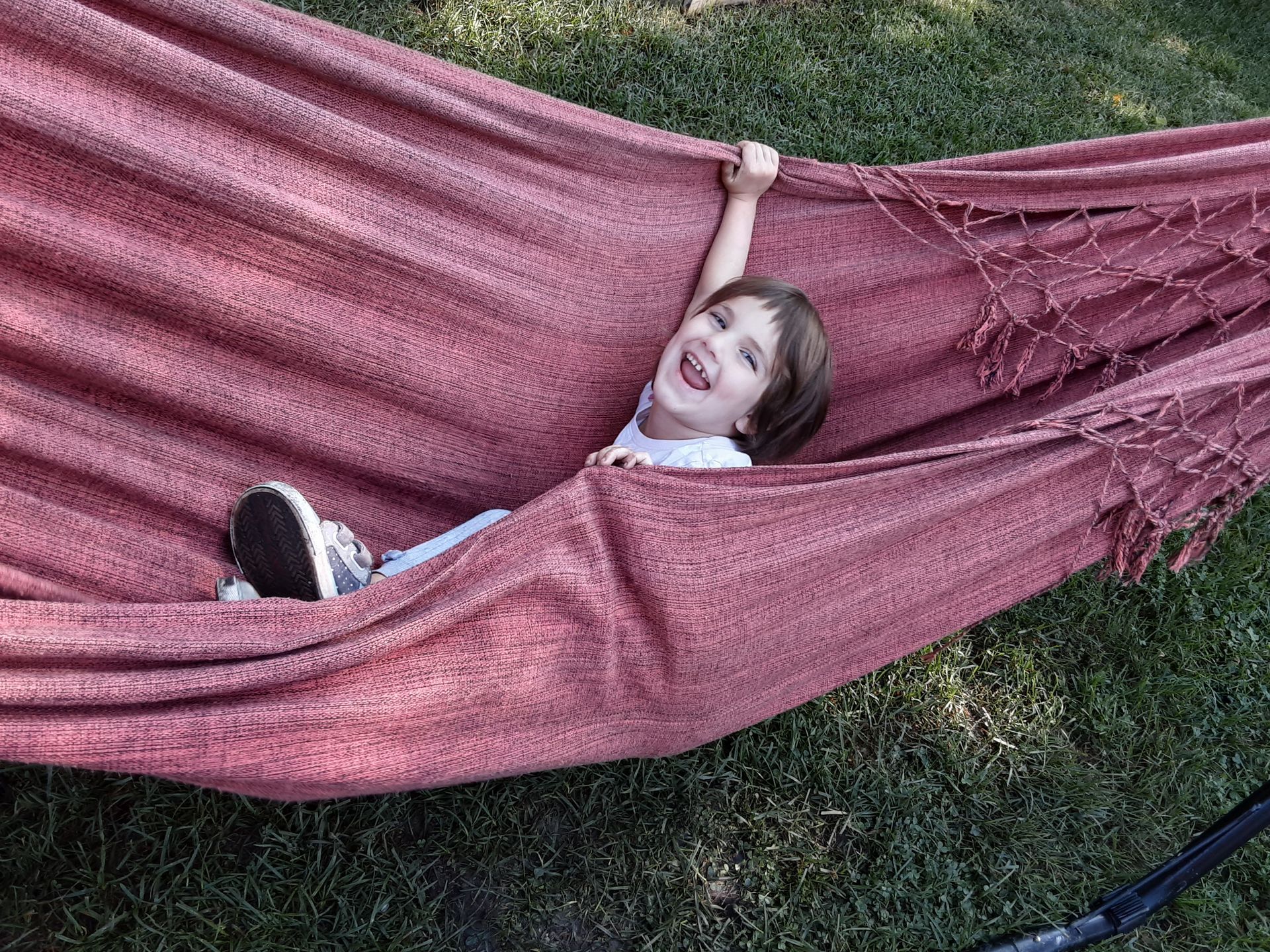 A smiling young child is in an outdor hammock.