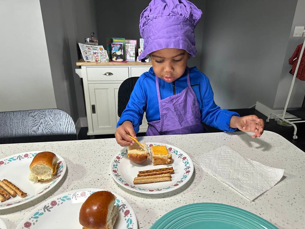 child with purple chef’s hat assembling lunch food on a plate
