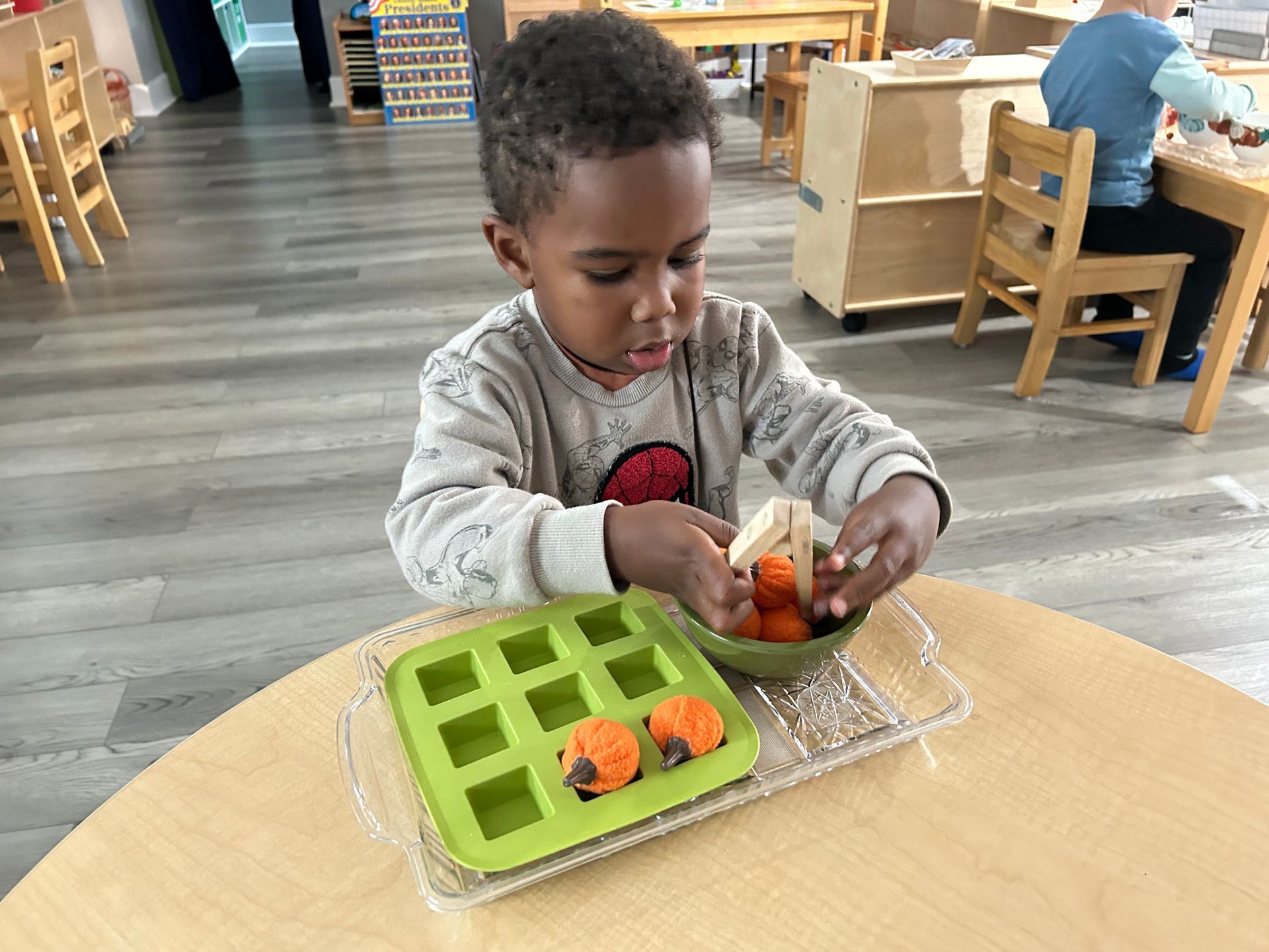 A child sorts small pumpkin decorations into a bright green tray.