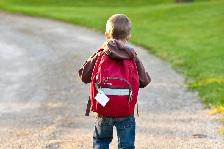 back of a child with red backpack who is walking down a driveway