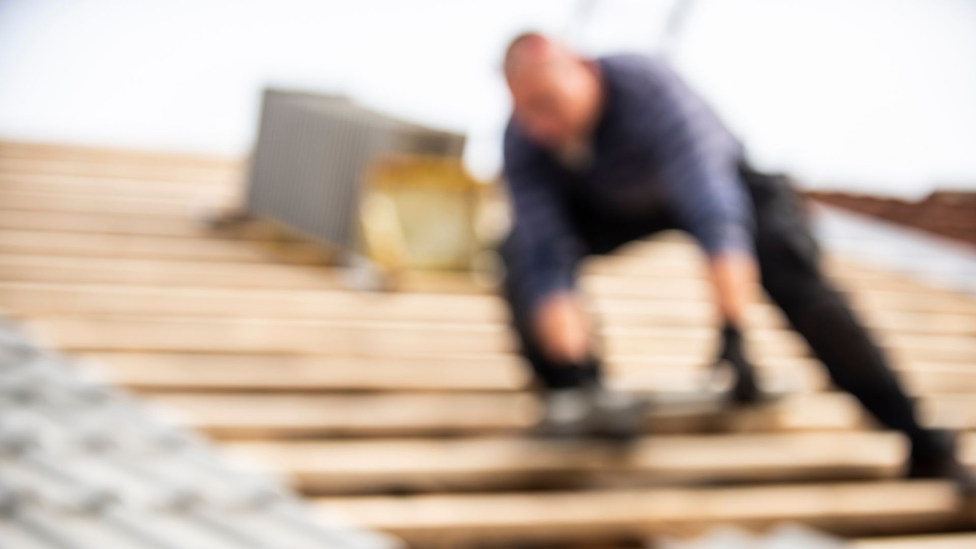 Blurred image of a roofer working on a wooden roof with tools.