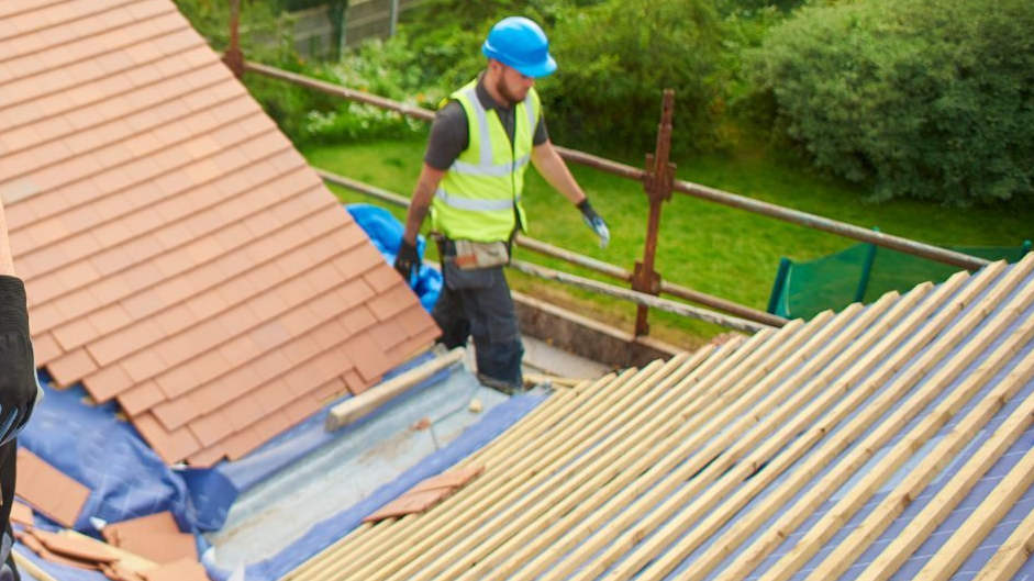 A worker torching roofing material on a flat roof; safety equipment is visible.