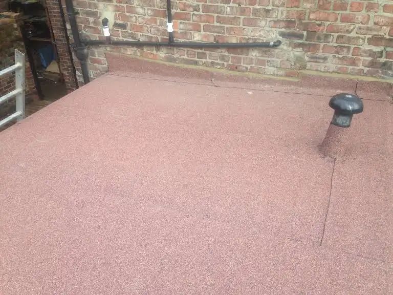 Red flat roof with vent pipe and brick wall background.