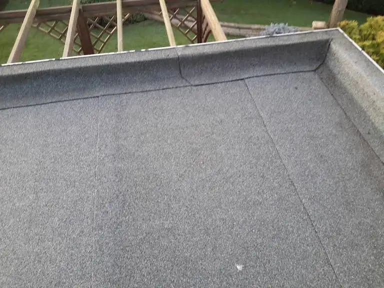 A gray flat roof with a raised edge, near a wooden structure and green grass.