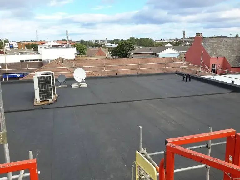 Flat, black rooftop with air conditioning unit, satellite dishes, and cityscape background.
