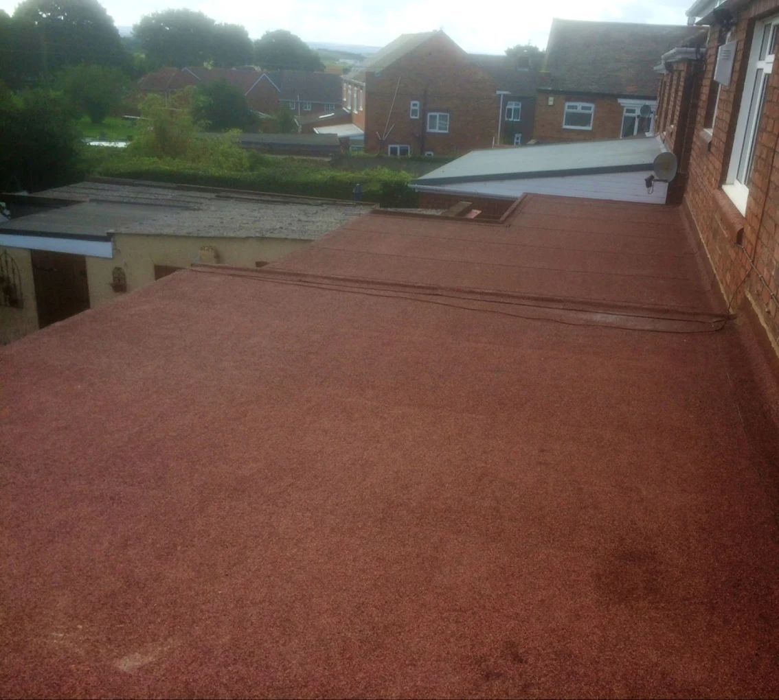 Red flat roof with surrounding buildings and greenery.